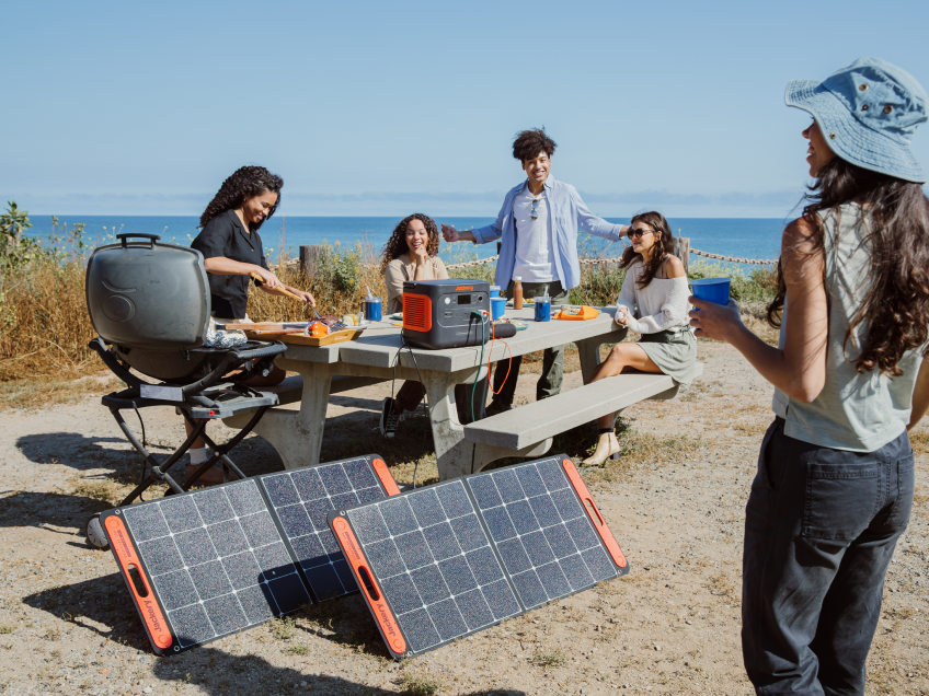 Friends with Jackery portable power and solar panels at a seaside picnic